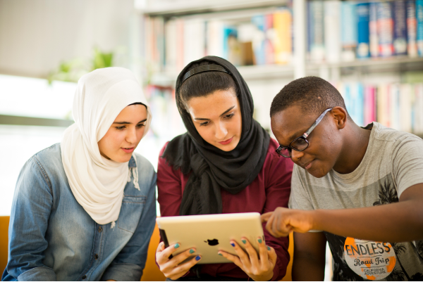 Three students looking at an iPad whilst sitting in a library