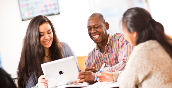 Three adults sitting at a table collaborating and working with an iPad.