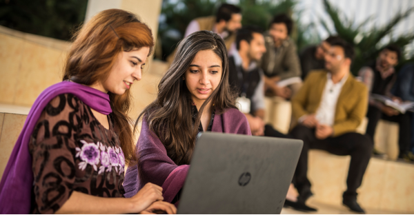 Two female students working on a laptop whilst sitting on steps