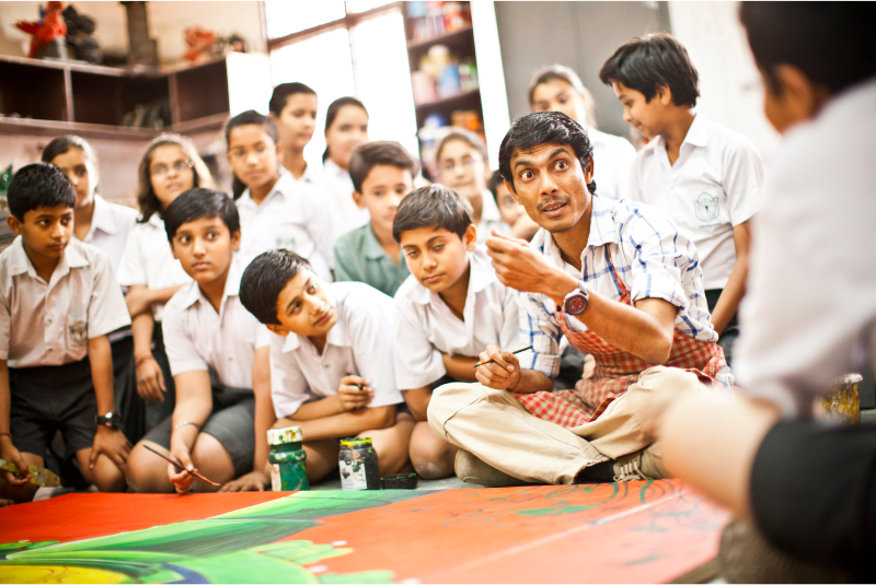 Teacher instructing a group of school boys in front a large painting in India